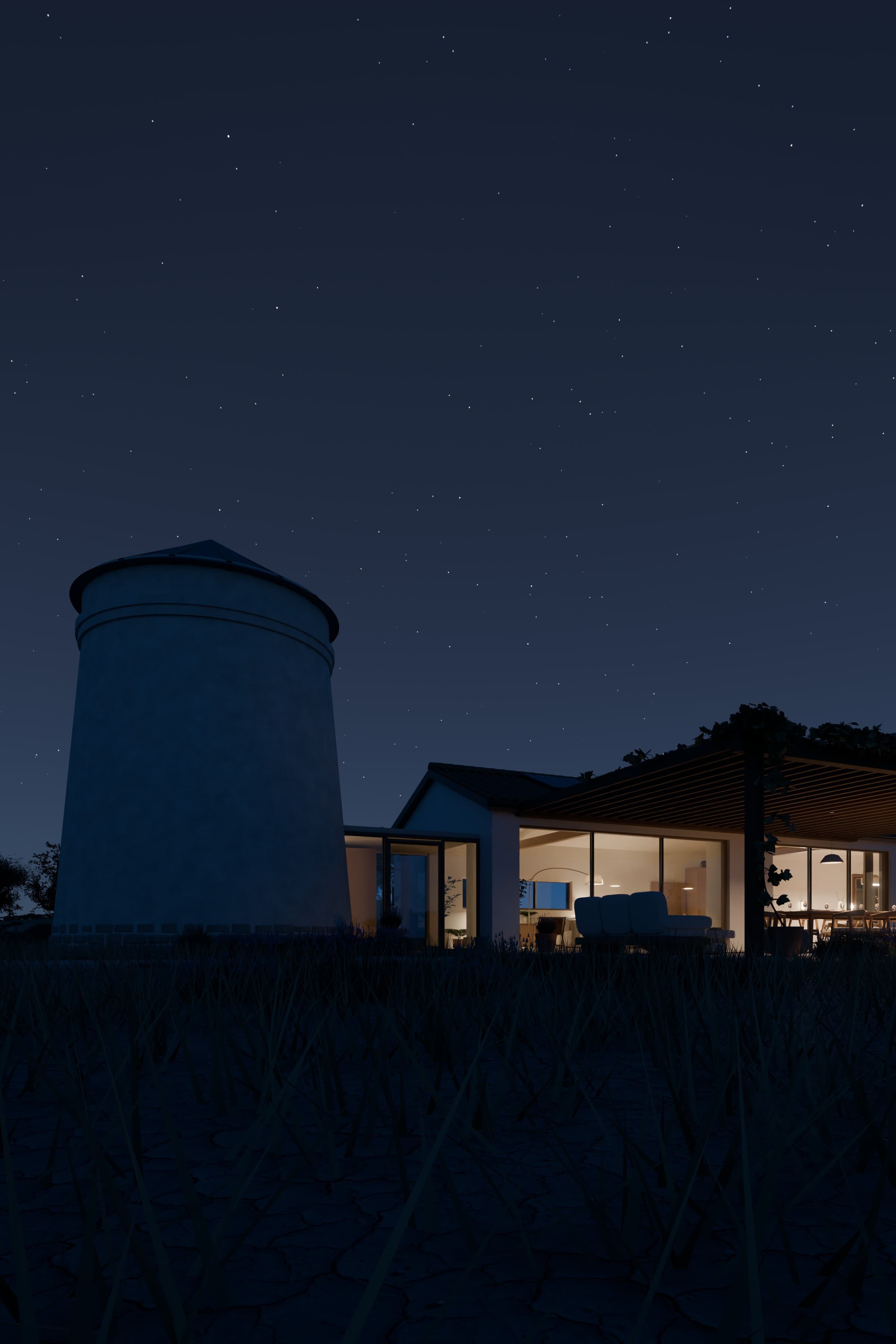 A whitewashed house with a converted windmill at dusk, its glazed living and dining rooms lit warmly under a vine-covered pergola, beneath a clear starry sky over a dry meadow.